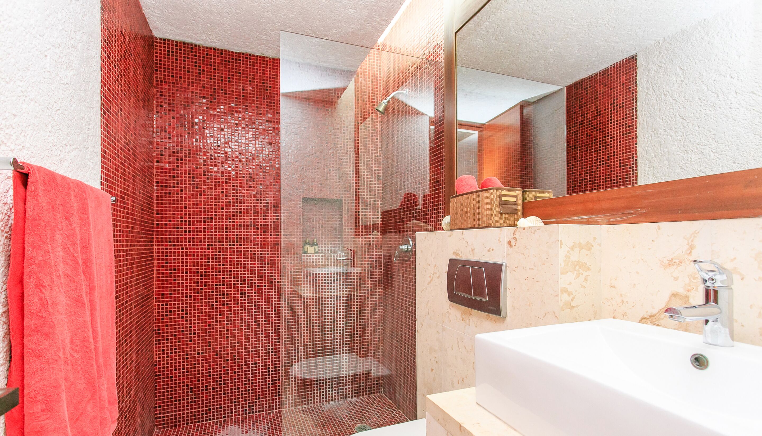 A bathroom with a red-tiled shower enclosure, a white sink, and a mirror above the sink.