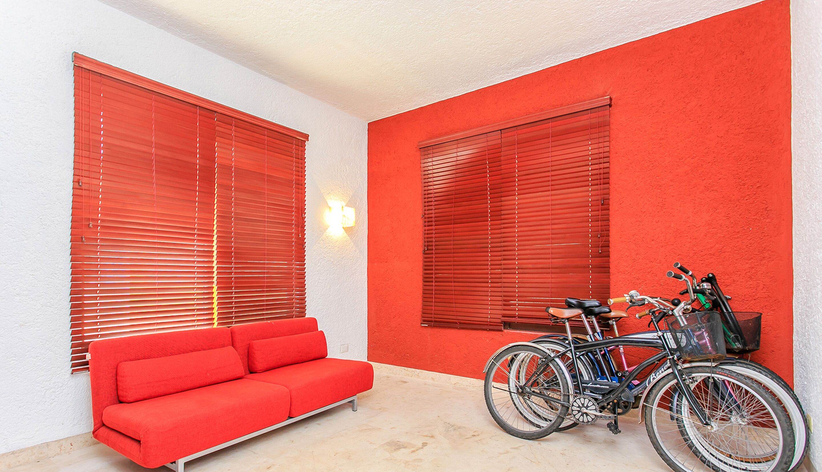 A room with a red sofa, two bicycles, and red blinds on the windows.