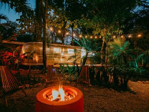 A cozy outdoor seating area with a fire pit, surrounded by chairs and a dining table, with a camper RV in the background.