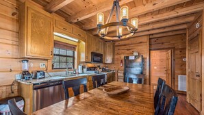 A wooden cabin interior with a dining table, chairs, a chandelier, wooden cabinets, a microwave, a refrigerator, and a dishwasher. - Eagle’s Crest at Mentone-Amazing Views, sleeps 8 (Mentone)