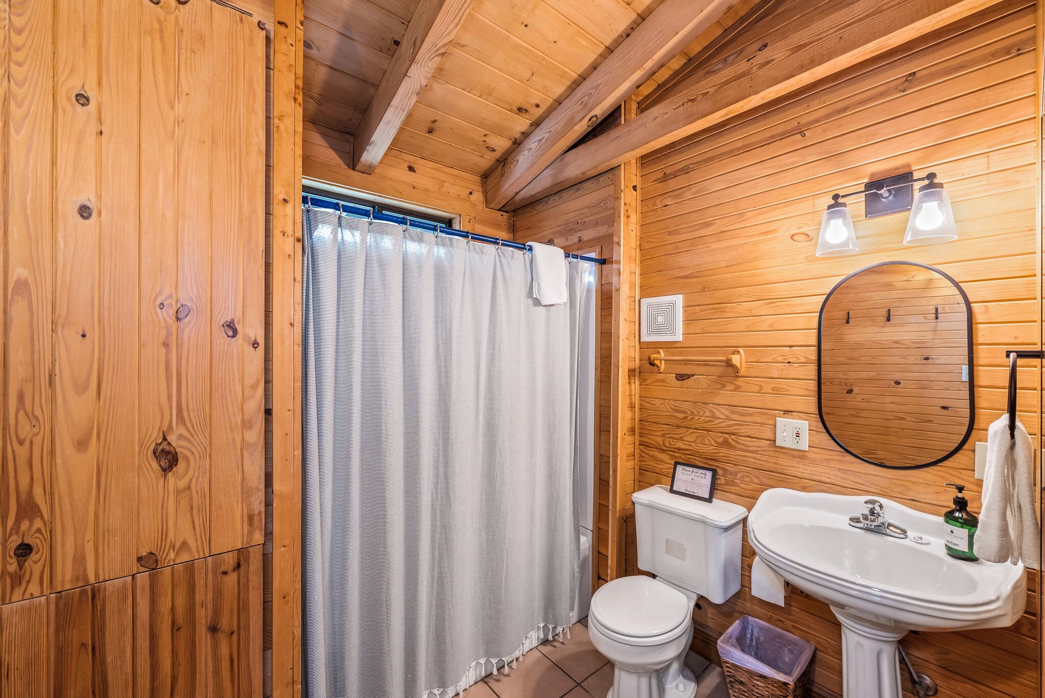 A wooden cabin bathroom with a shower curtain, toilet, sink, and mirror.