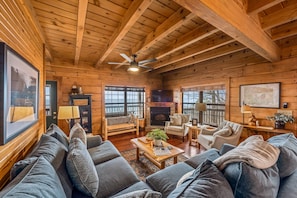 A cozy log cabin interior with a fireplace, wooden furniture, and large windows.
