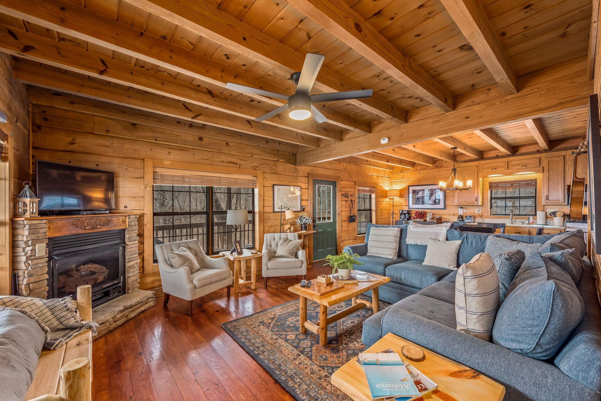 A cozy log cabin interior with a fireplace, comfortable seating, and a ceiling fan.