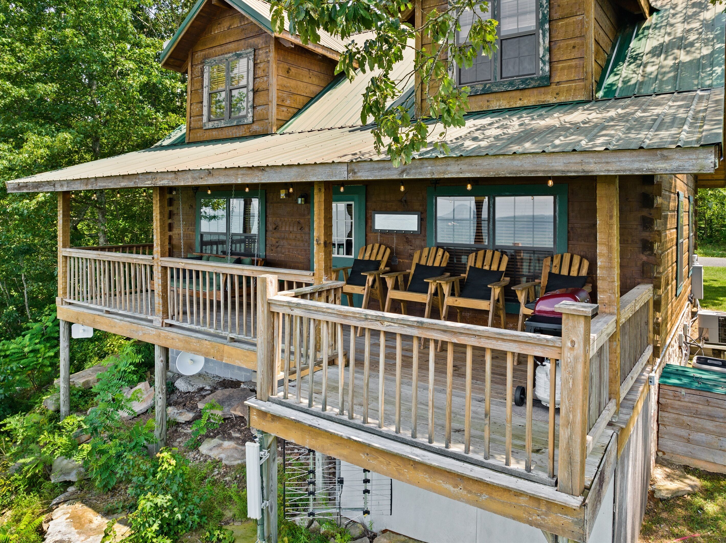 A wooden cabin with a balcony, outdoor seating, and a view of the surrounding greenery.
