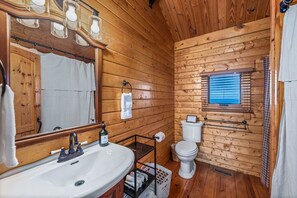 Un baño de cabaña de madera con lavamanos, espejo y inodoro.