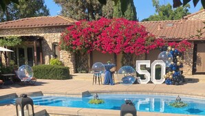 A pool area with a stone building, a large '50' sign, and pink bougainvillea flowers. - Vineyard suite located in the orchard with private entrance-Villa Riposo Winery (Morgan Hill)