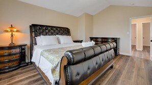 A bedroom with a large bed, a nightstand, a lamp, and a dresser.