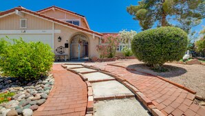 A house with a garage, a paved driveway, and a well-maintained garden with a variety of plants and a large tree.