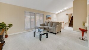 A spacious living room with a glass coffee table, beige walls, a sofa, and a staircase leading to another level.