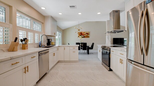 A modern kitchen with white cabinetry, stainless steel appliances, and a dining area with black chairs and a table.