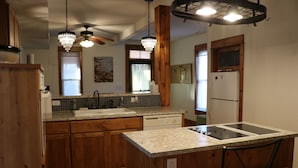 A kitchen with wooden cabinets, a granite countertop, a built-in dishwasher, and a ceiling fan.