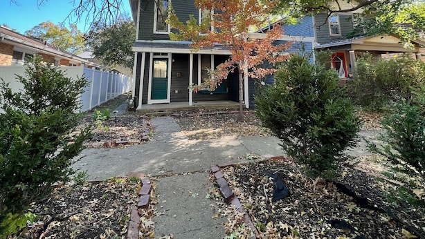A residential house with a front porch, a driveway, and a garden area with fallen leaves.