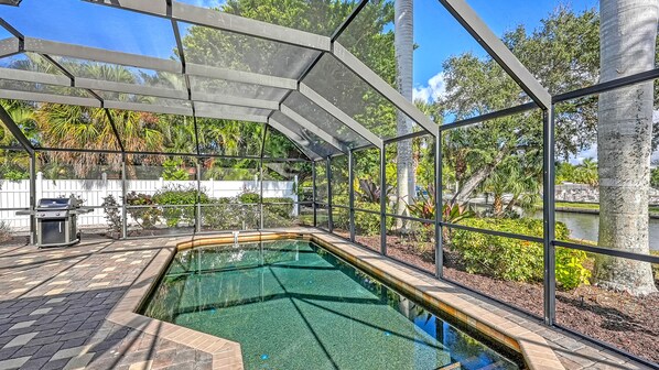 Piscina com cobertura de vidro, cercada por vegetação e área com churrasqueira.
