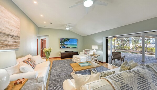 A spacious living room with a large flat-screen TV, comfortable seating, and a view of a pool and outdoor area. - Bali Hai House | Canal-Front Home with Private Heated Pool, Near Siesta Key Village (Siesta Key)