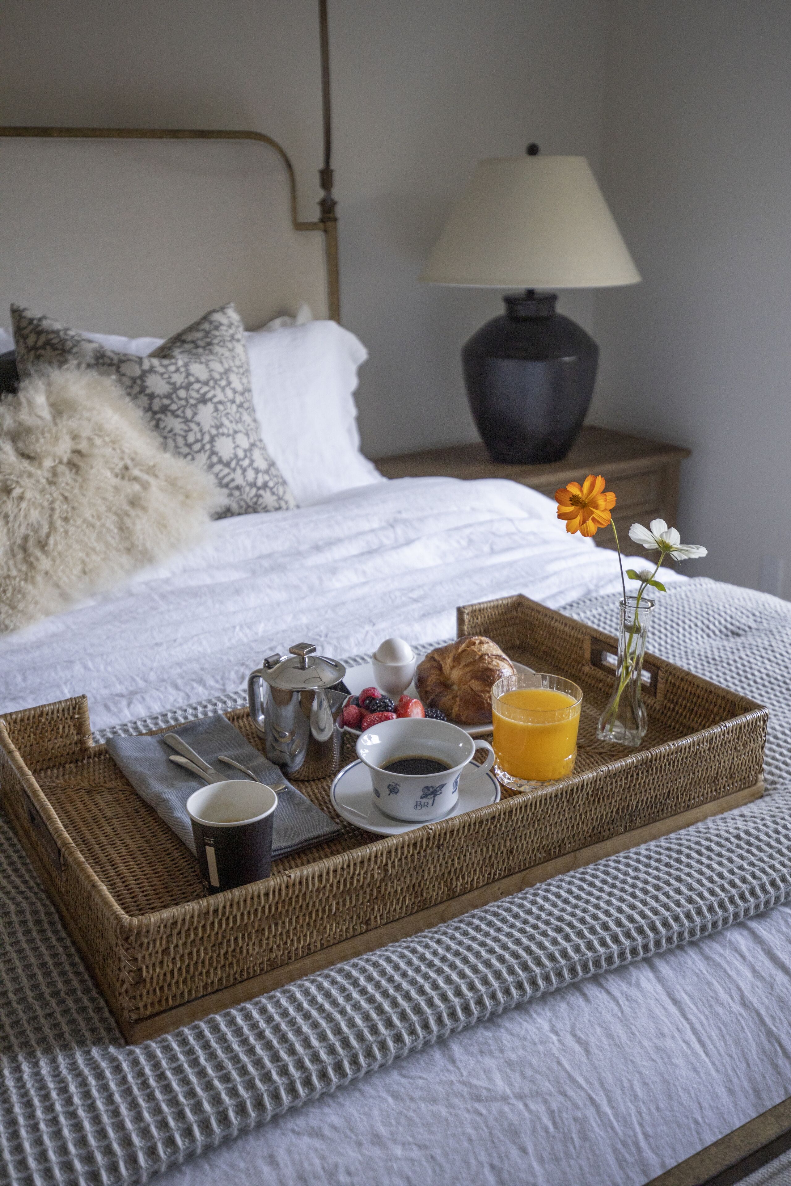 A neatly made breakfast tray on a bed with a lamp, flowers, and a cup of coffee.