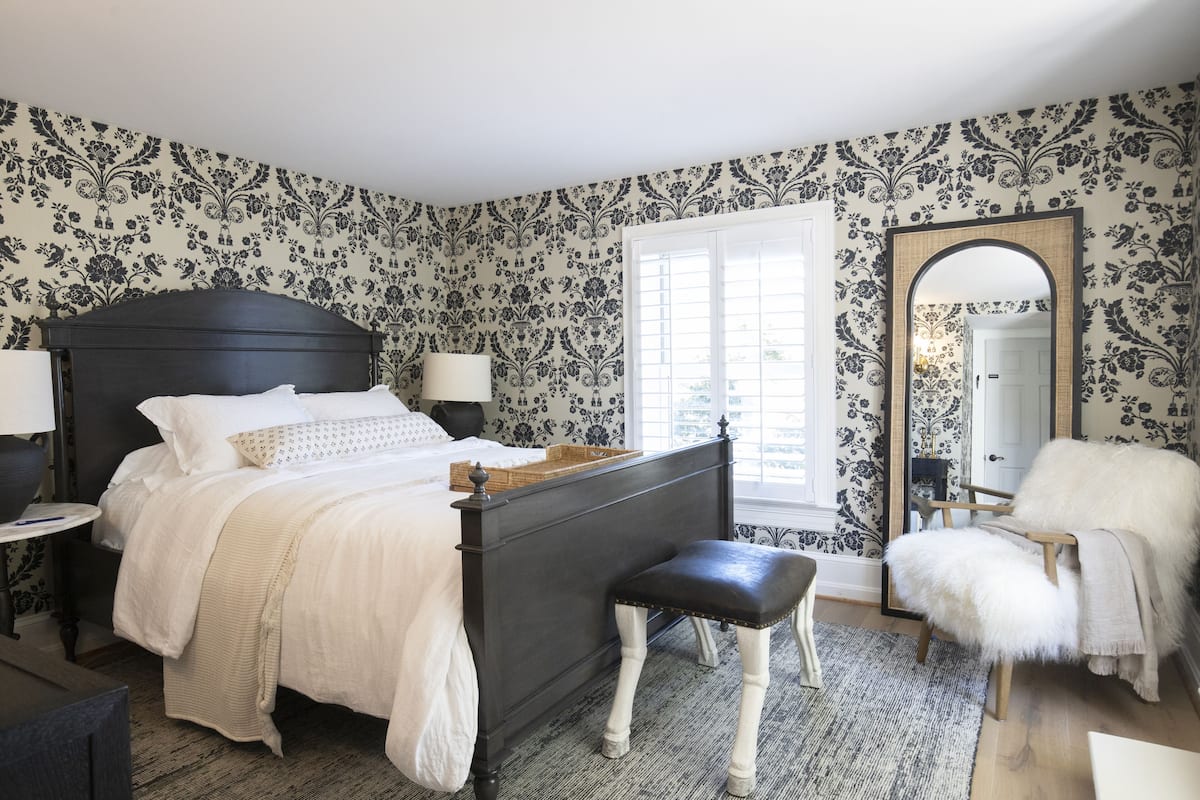 A bedroom with a dark wooden bed, white bedding, a bench, a chair, and a large mirror.