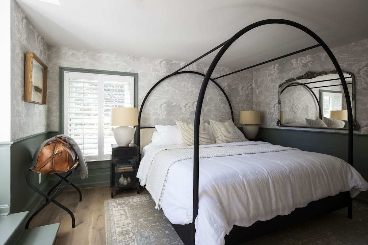 A bedroom with a four-poster bed, a bench with a bag, and a large mirror.