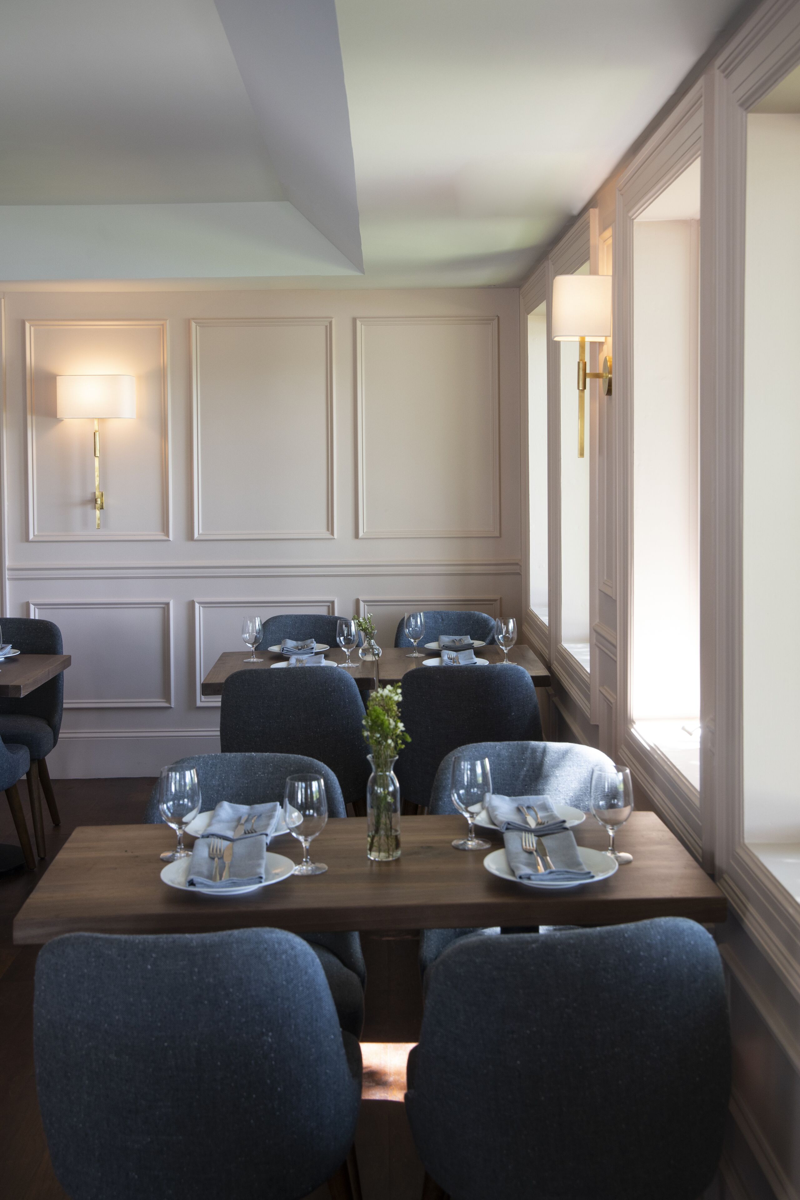 A dining area with a long table set for six, surrounded by chairs, with a vase of flowers in the center.