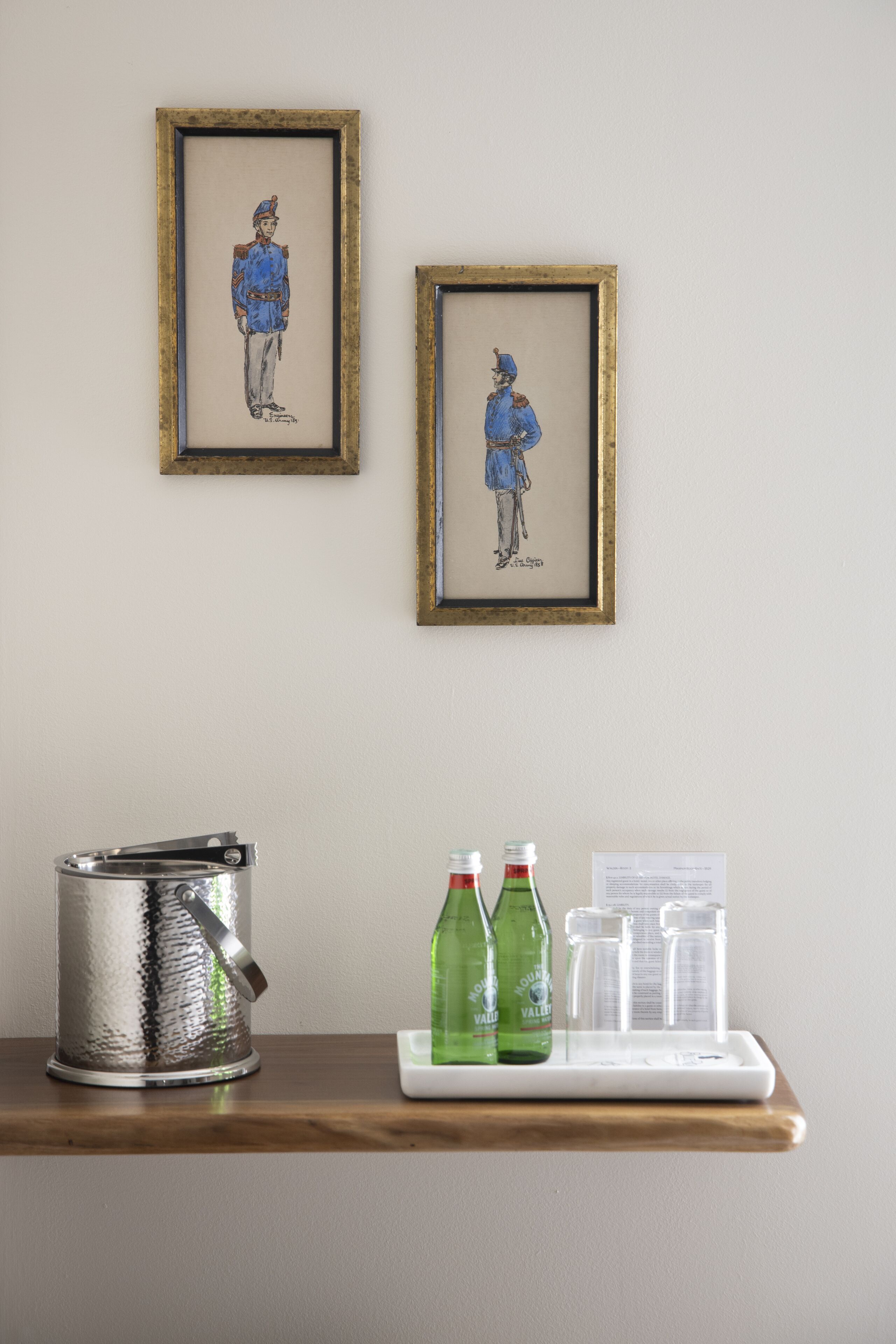 A framed artwork on the wall, a metal container, and a tray with bottles and glasses.