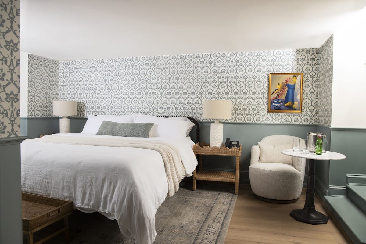 A neatly arranged bedroom with a bed, bedside tables, a chair, and a small table with a bottle.