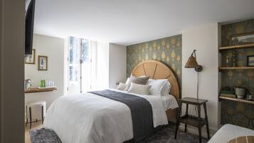 A neatly arranged bedroom with a large bed, a bedside table, a lamp, and a shelf with decorative items.