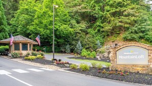 A landscaped entrance with a stone sign for MountainLoft, a small building with American flags, and a flagpole. - MountainLoft™ - 2 Bedroom Combined Lodge (Gatlinburg)