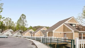 A row of single-story cabins with a covered walkway, surrounded by trees and a clear sky. - MountainLoft™ - 2 Bedroom Combined Lodge (Gatlinburg)