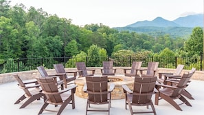 A circular seating arrangement with chairs around a central fire pit, set against a backdrop of lush greenery and distant mountains.