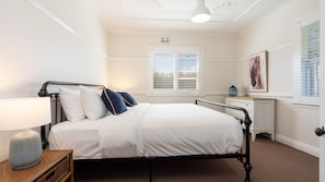 A bedroom with a bed, bedside table, lamp, and a window with blinds. - Hanigan's Cottage Connect with the country (BOLONG)