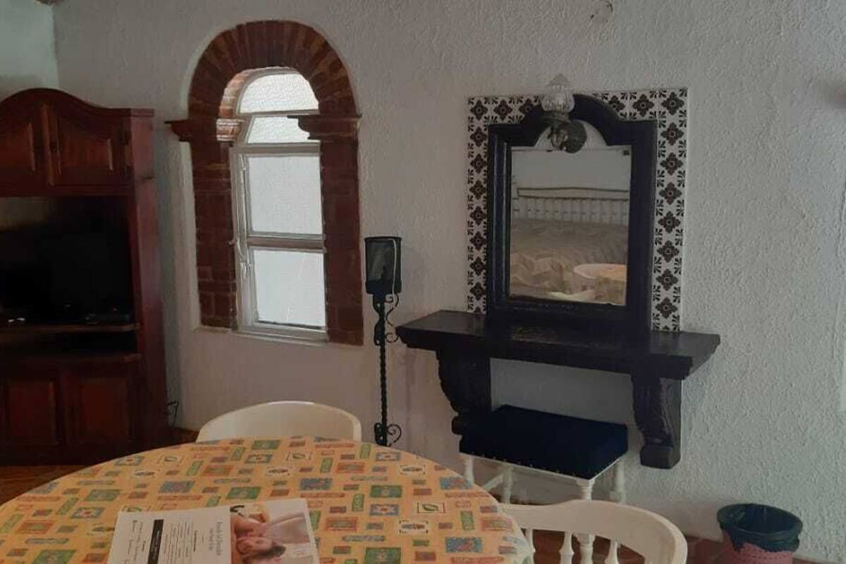 A dining area with a round table, chairs, a wooden cabinet, a television, and a wall-mounted shelf with a mirror.