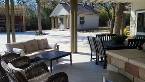 An outdoor patio area with a covered seating area, a small table, and a trash can. - Country guesthouse w/ shared pool, firepit, and outdoor kitchen access (Lexington)