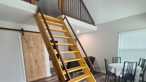 A wooden staircase leading to an upper floor, a dining area with a round table and chairs, and a large window with blinds. - Country guesthouse w/ shared pool, firepit, and outdoor kitchen access (Lexington)