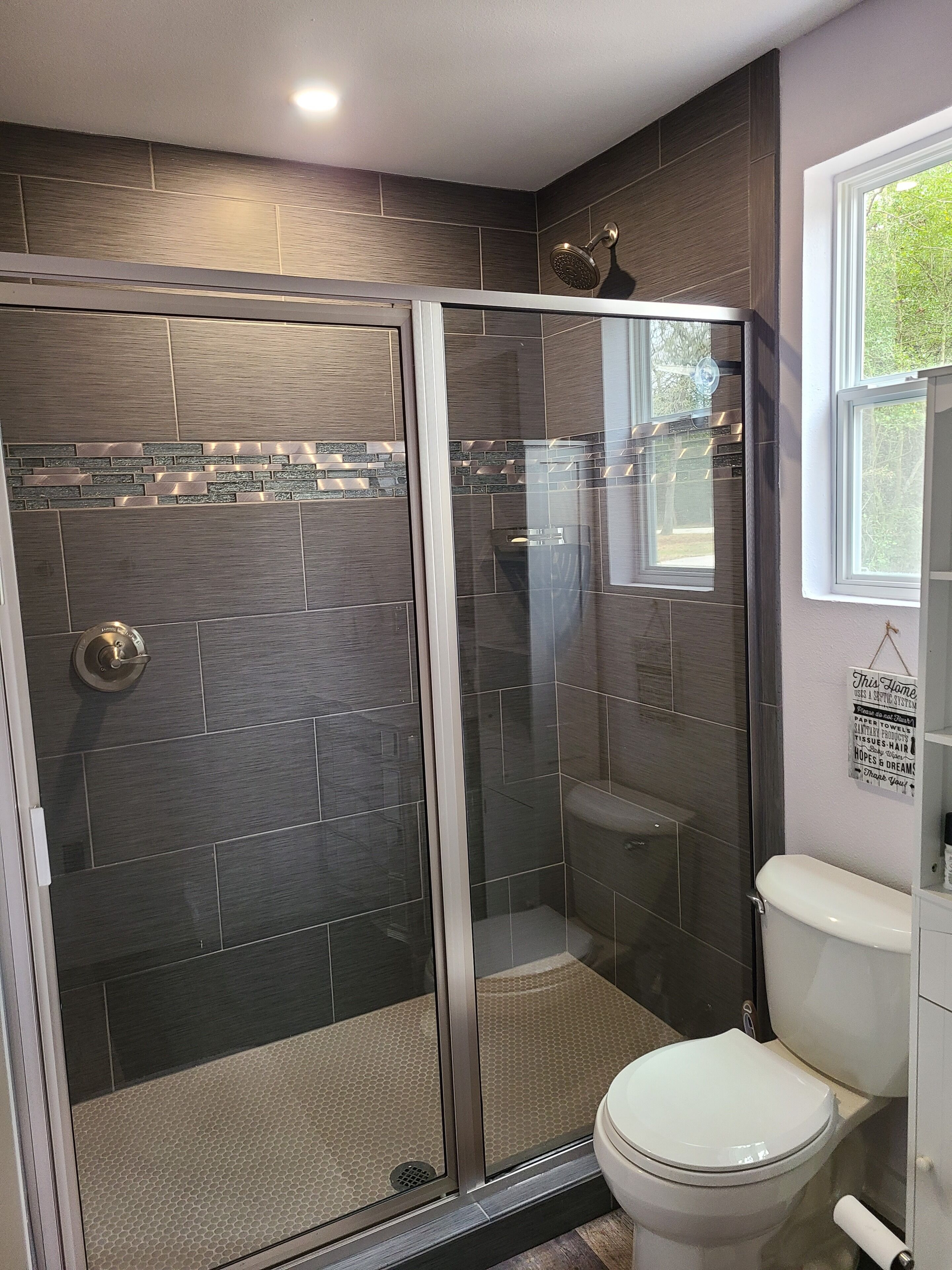 Une salle de bain moderne avec une douche à parois de verre, des murs recouverts de carreaux foncés et des toilettes blanches.