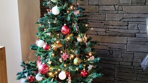 Ein mit Schmuck und Lichterketten geschmückter Weihnachtsbaum vor einer Steinwand.