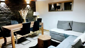 Ein modernes Wohnzimmer mit einem Holzesstisch, schwarzen Stühlen, einem grauen Sofa und einem kleinen Holzschemel.