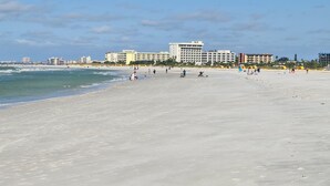 Una spiaggia ampia con cielo sereno, alcune persone e edifici sullo sfondo.