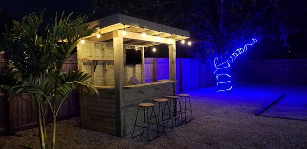 Un bar extérieur en bois doté d’un espace salon couvert et de tabourets.