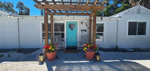 A building with a wooden pergola entrance, a turquoise door, and potted flowers.