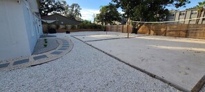 Un jardin avec un filet de volley-ball, un barbecue et un petit espace aménagé en potager.