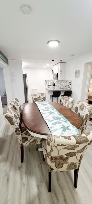 Enjoy meals in this dining area with a long table and comfortable chairs, surrounded by a kitchen with a microwave and sink.