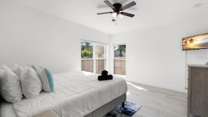 Una camera da letto con un letto, una ventola a soffitto, una finestra e un quadro al muro.
