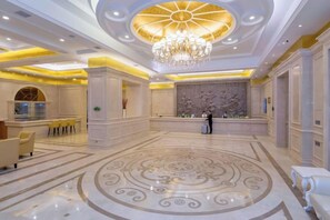 A spacious lobby with a large chandelier, a reception desk, and a decorative wall.