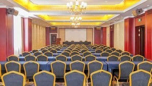 Un salón de conferencias con mesas y sillas dispuestas en filas, un atril y una pantalla grande al frente.