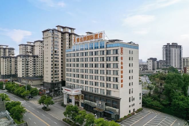 A multi-story hotel with a prominent sign, surrounded by other buildings and greenery.