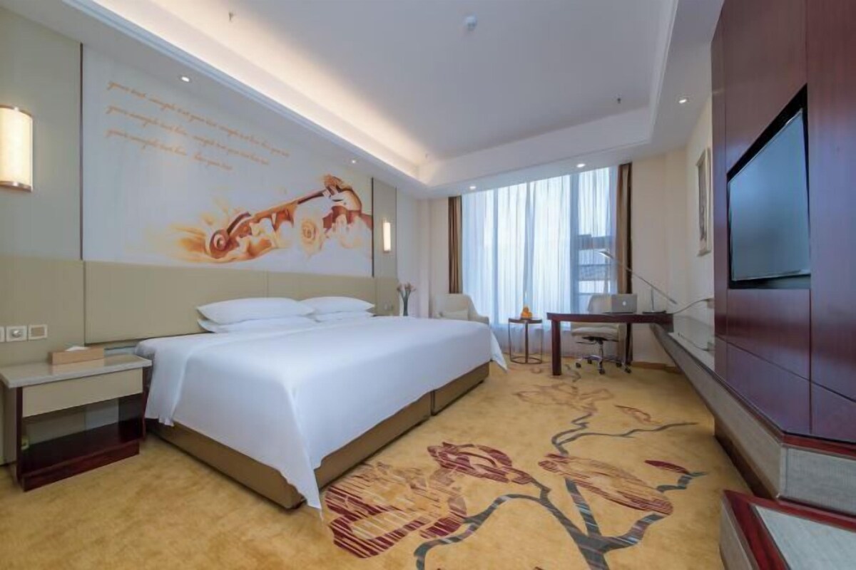 Habitación de hotel con una cama grande, un escritorio con silla, un televisor y un mural decorativo en la pared.