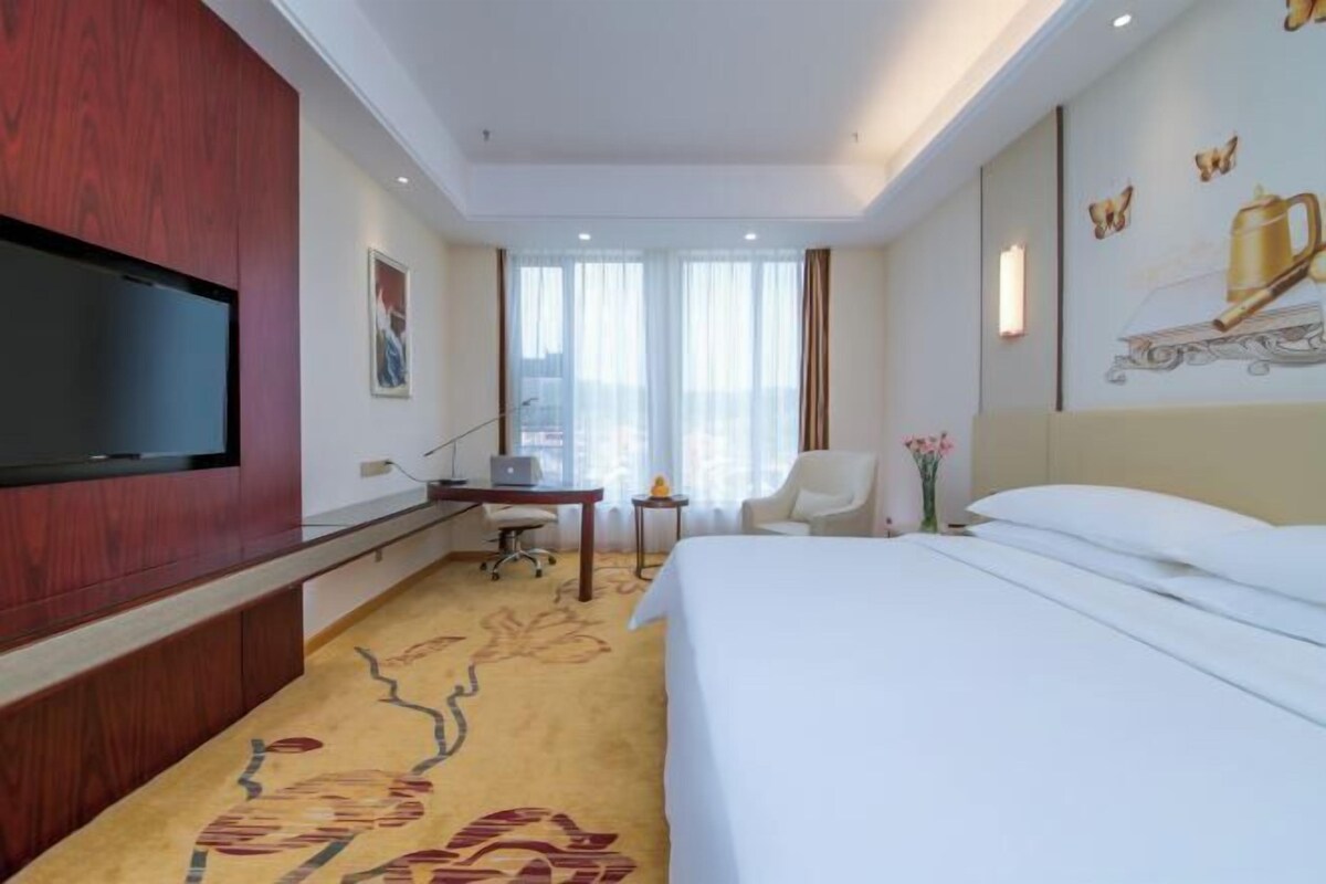 Habitación de hotel con cama, escritorio, silla, televisor y vista a la ciudad.