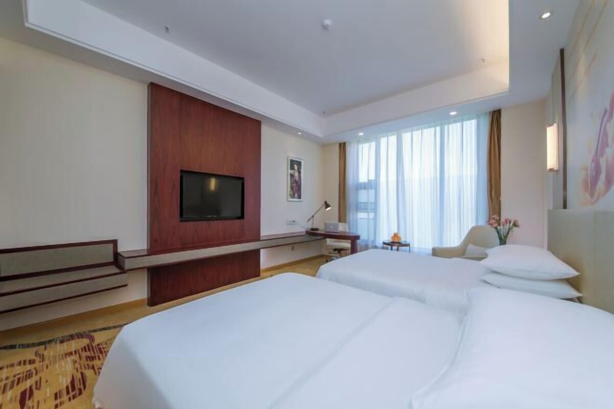 Habitación de hotel con dos camas, televisor, escritorio y ventana con cortinas.