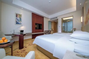 Una habitación de hotel con cama, escritorio, silla, televisor y un cuadro en la pared.