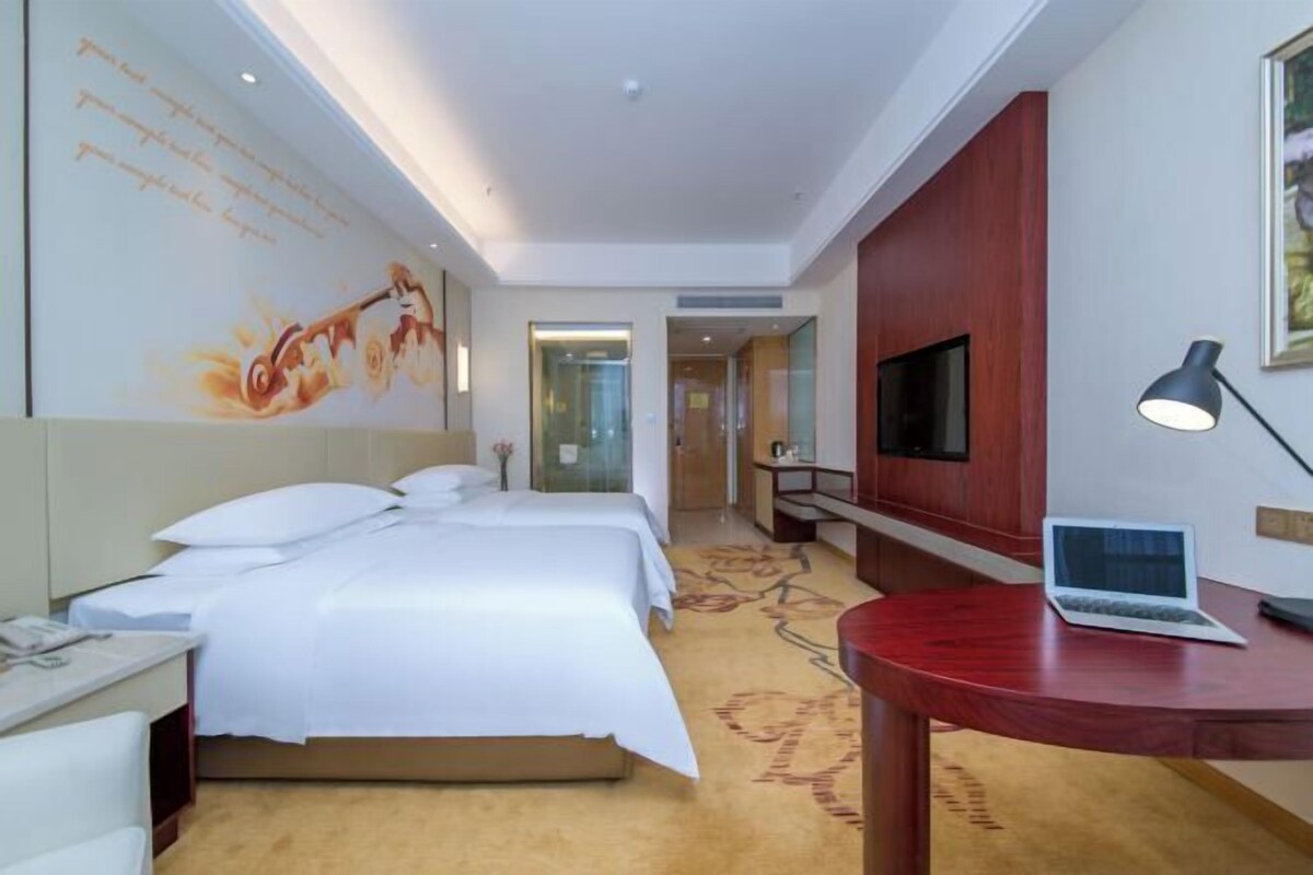 Habitación de hotel con cama, escritorio, computadora portátil, televisor y un mural en la pared.