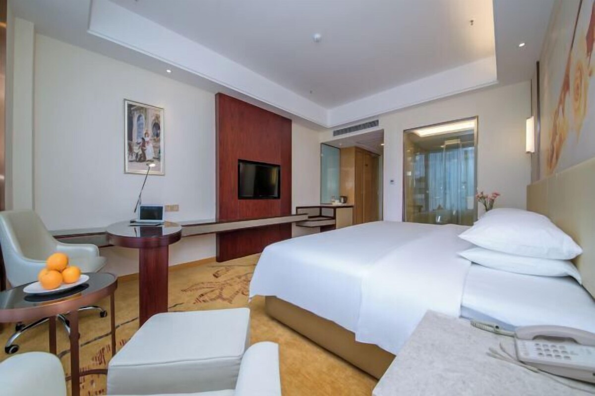 Habitación de hotel con cama, escritorio con computadora, silla, pequeña mesa con naranjas y teléfono en la mesita de noche.